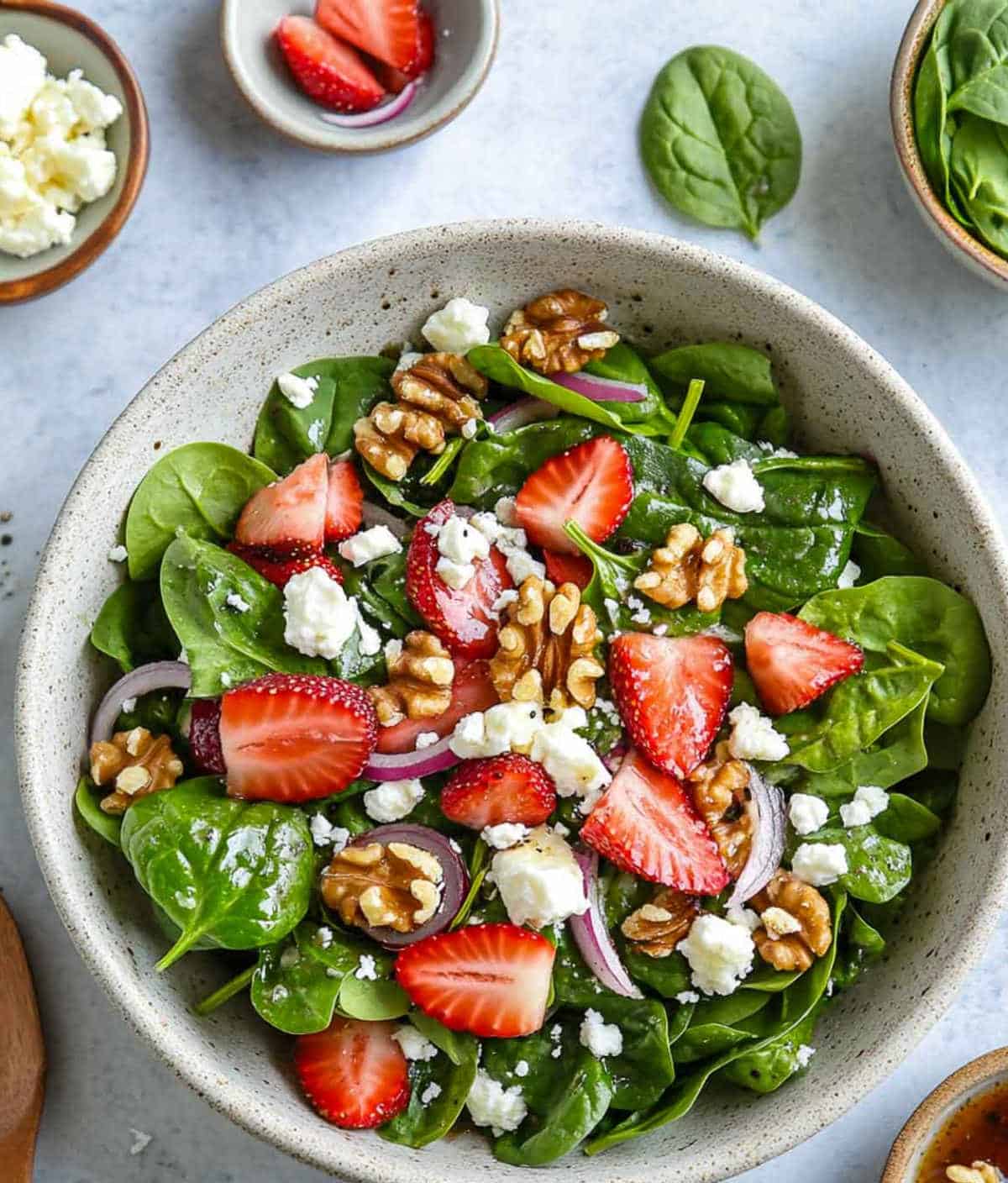 Side view of strawberry spinach salad with wooden handle in the background.