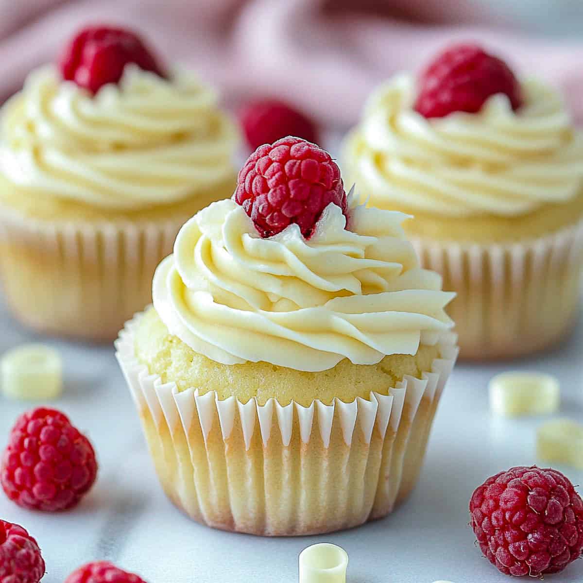 White chocolate and raspberry cupcakes on a marble surface.