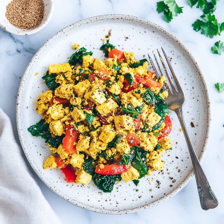 A plate of tofu scramble with bell peppers and spinach, served on a white marble surface with a fork on the side.