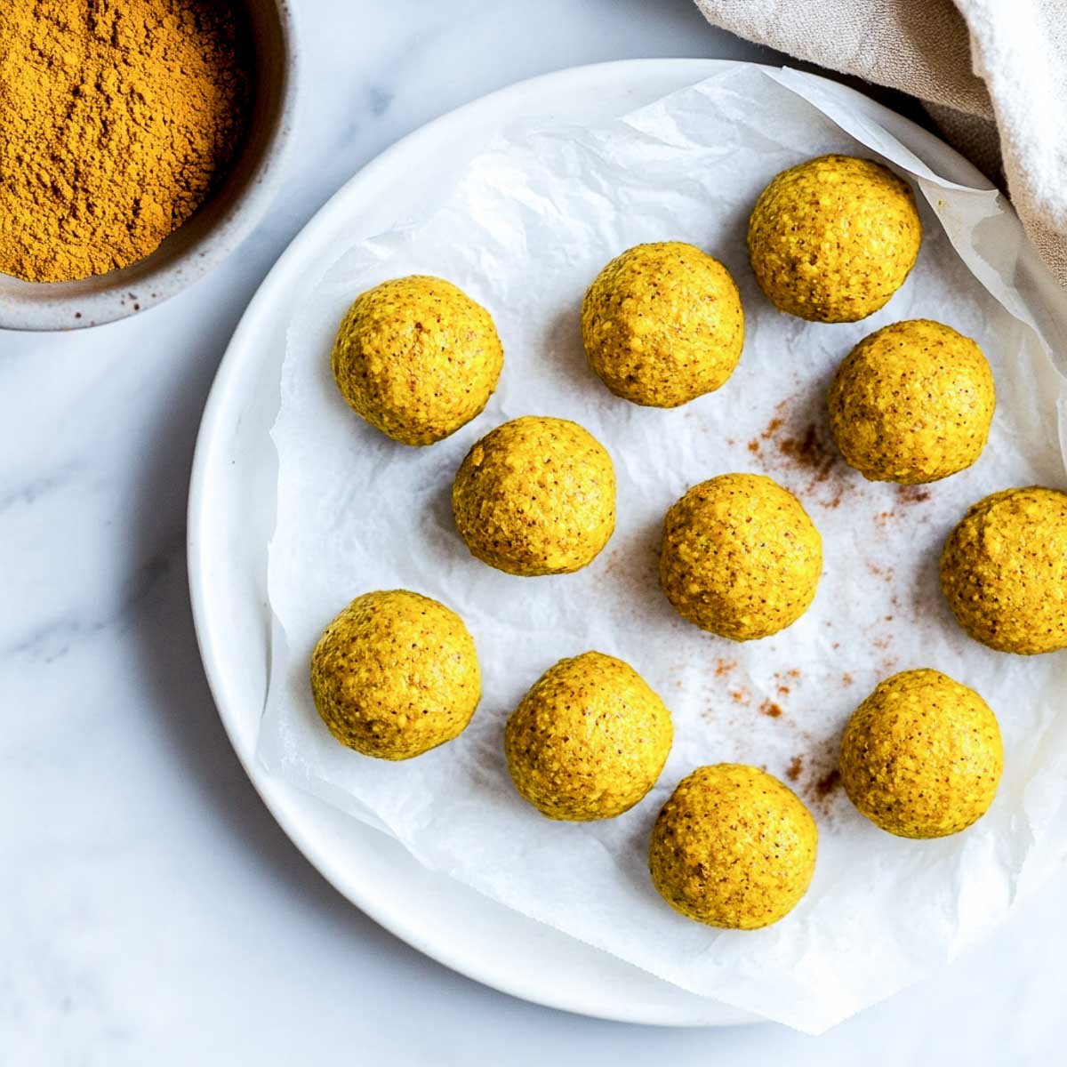 Turmeric protein bites served on a white plate with a bowl of turmeric in the background.