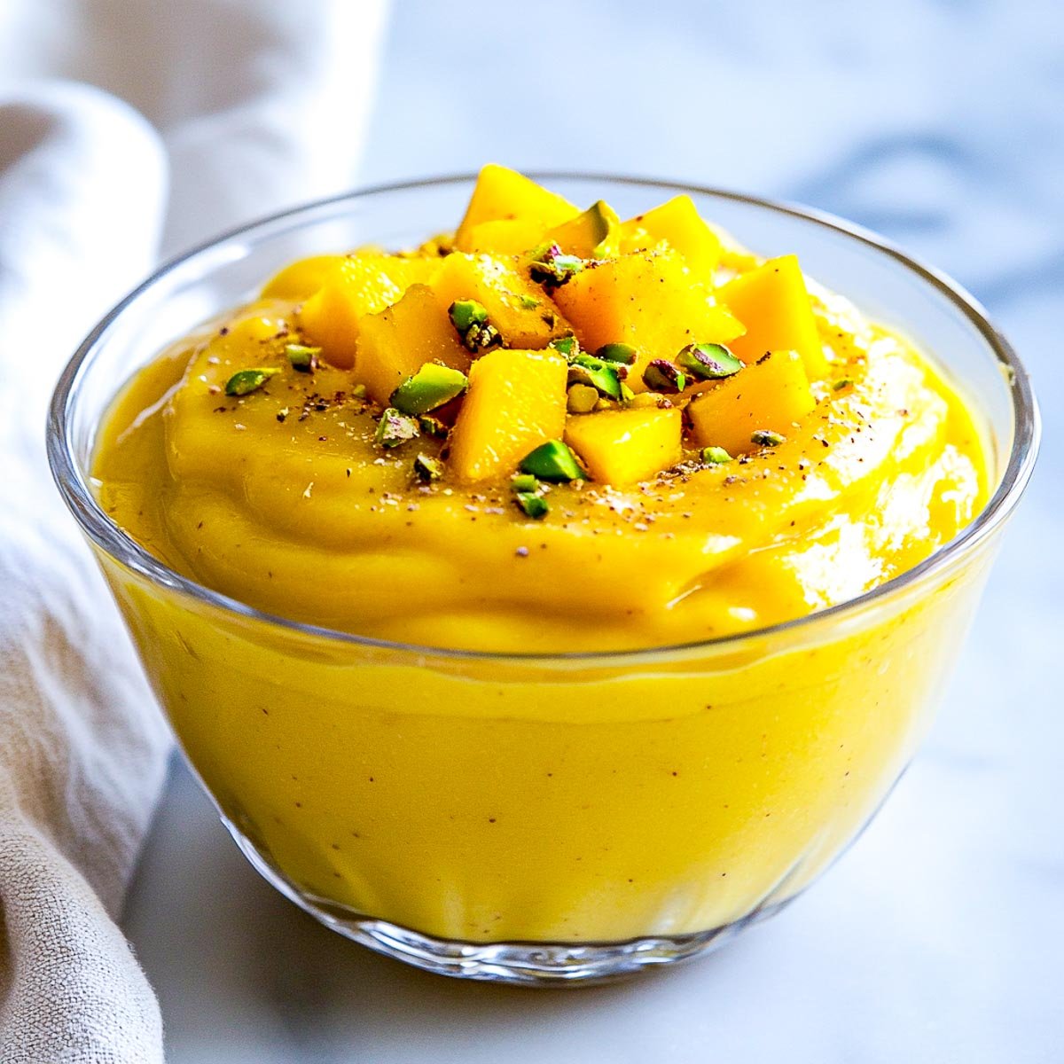 A bowl of creamy mango lassi pudding topped with pistachio.