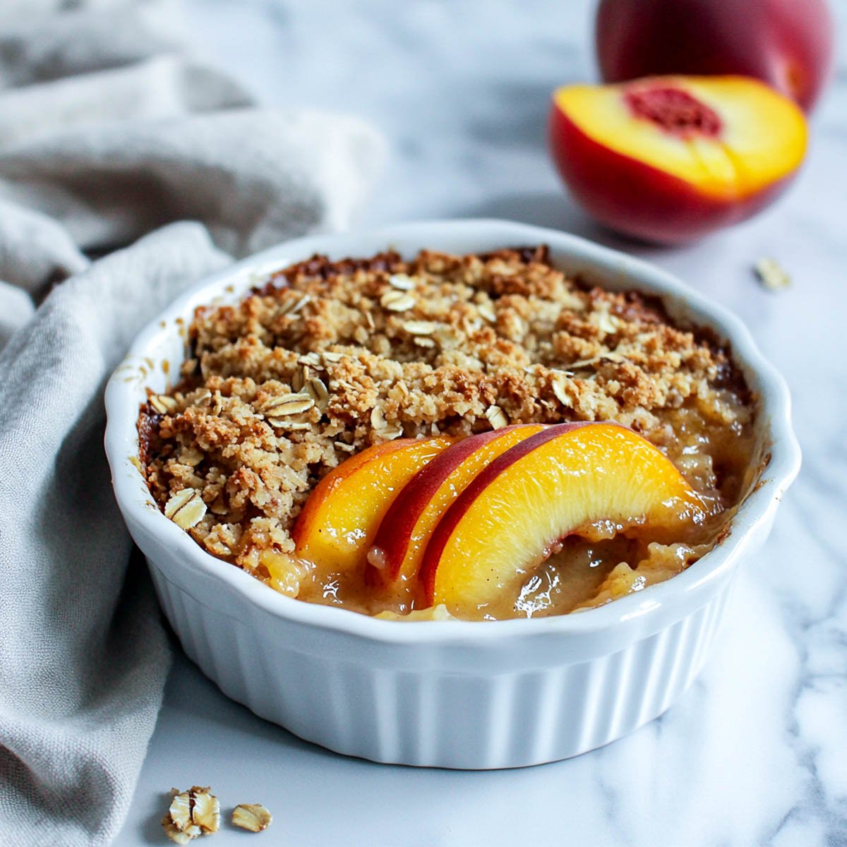 A bowl of peach crumble on a white marble surface.