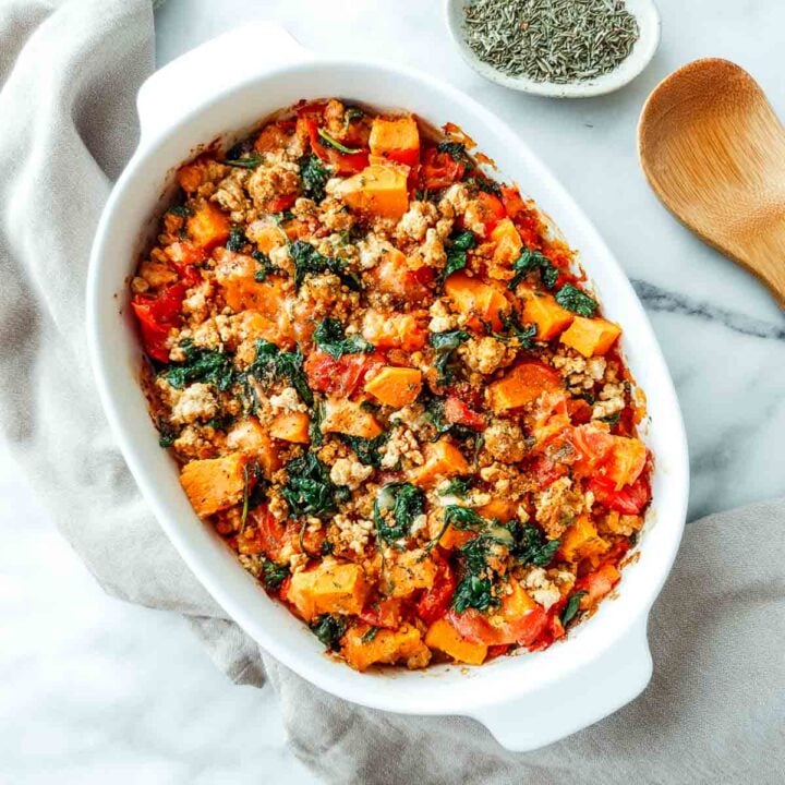 Baked turkey sweet potato casserole with spinach and tomatoes in white dish.