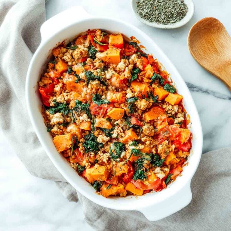Baked turkey sweet potato casserole with spinach and tomatoes in white dish.