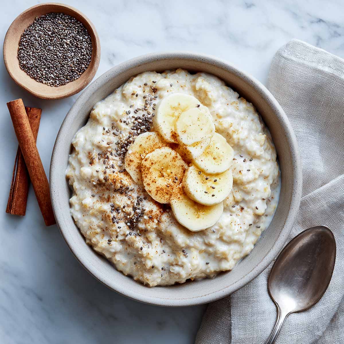 Bowl of creamy banana oatmeal topped with chia seeds and sliced banana for low calorie high protein breakfast.