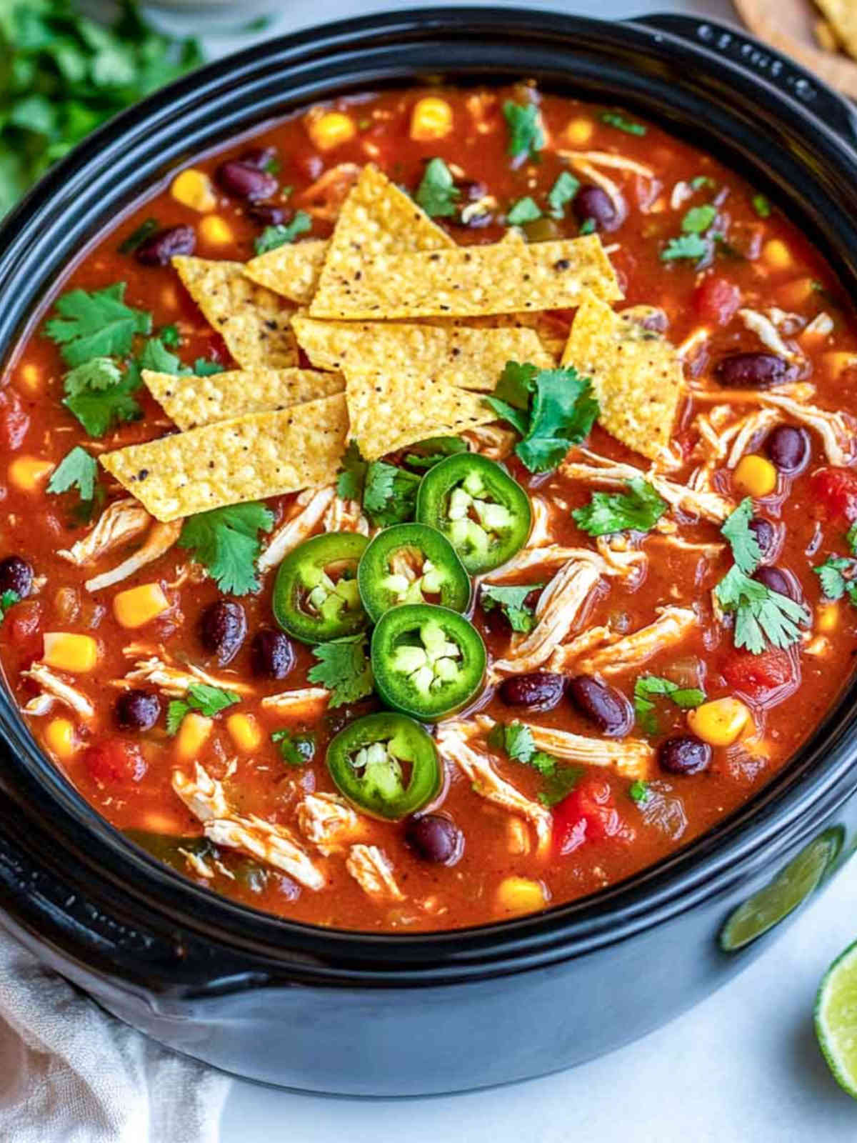 Close-up of chicken tortilla soup in a slow cooker with corn, beans, shredded chicken, cilantro, and jalapeños.