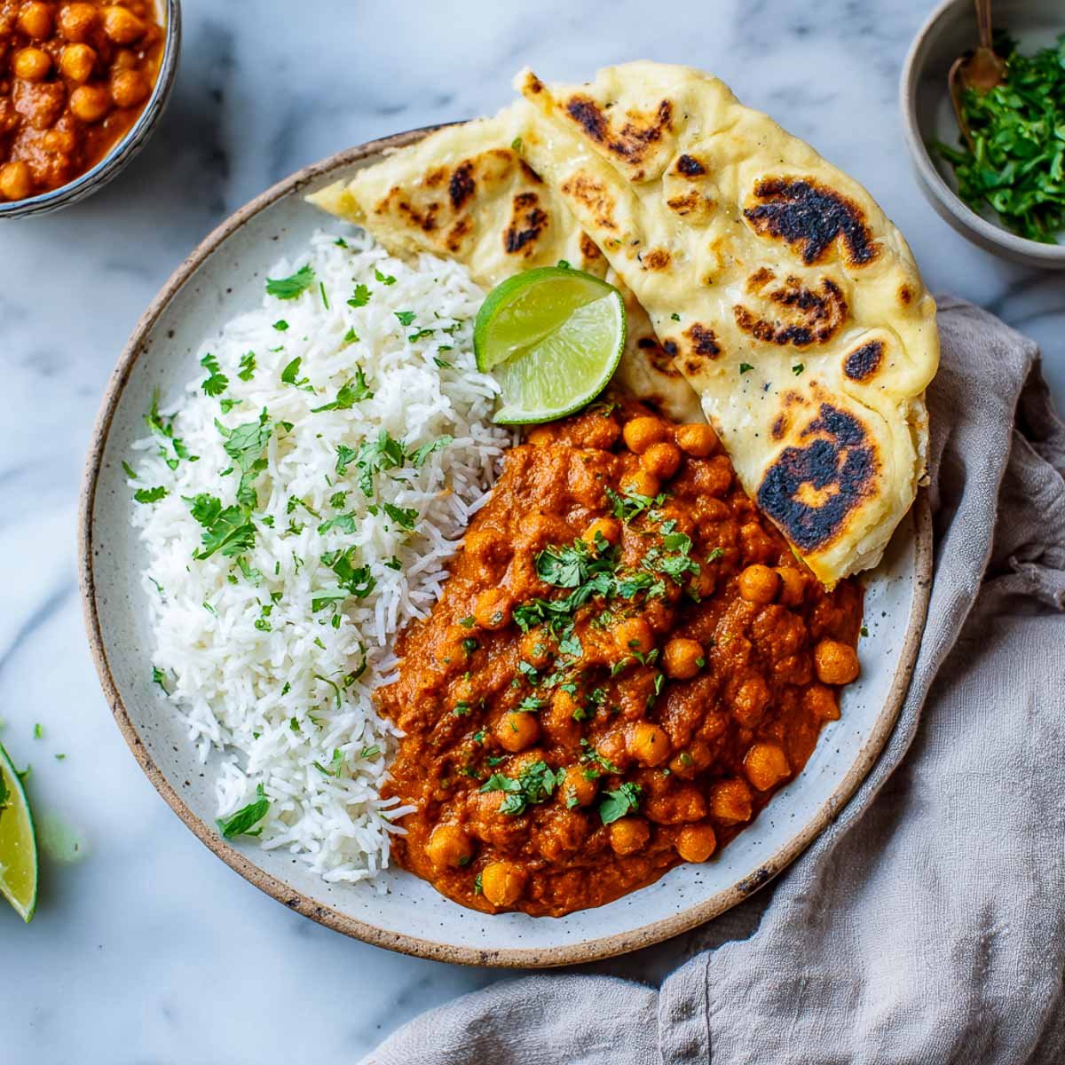 Plate of chickpea tikka masala served with basmati rice, naan, and lime wedge on a neutral ceramic dish.