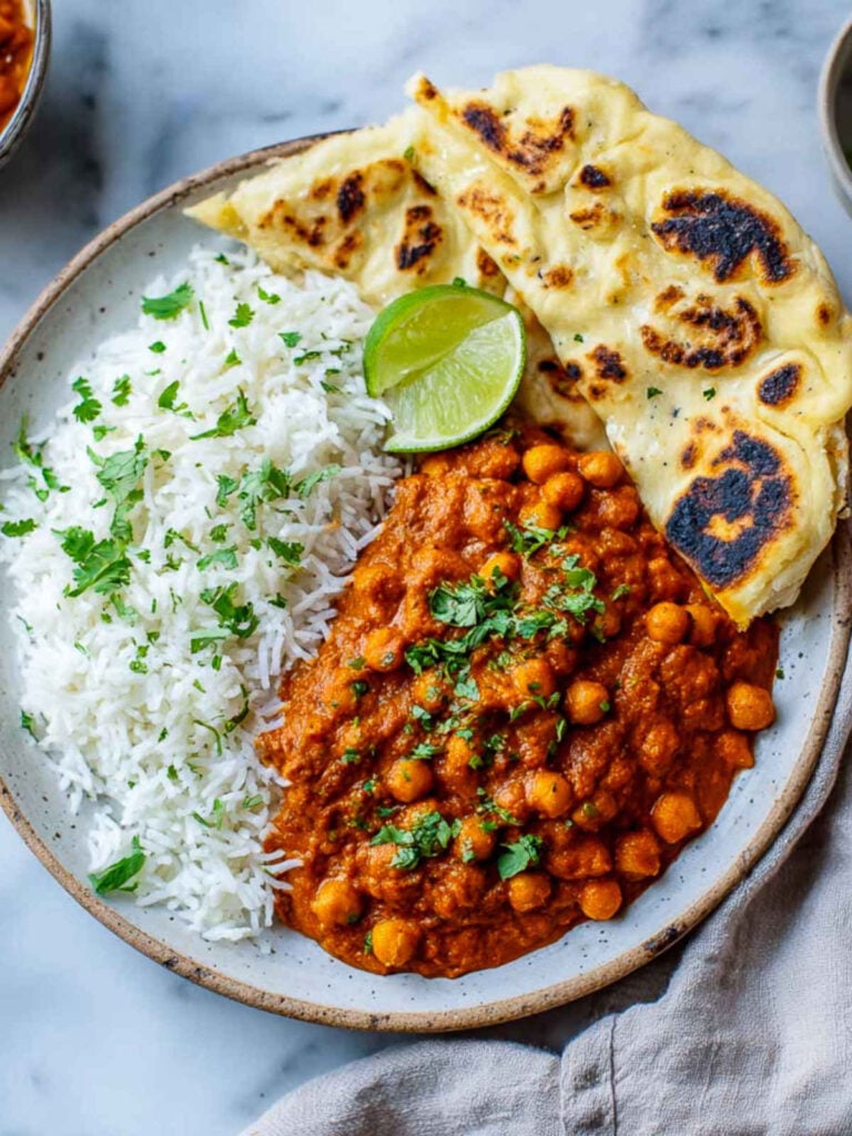 Close-up top view of chickpea tikka masala with rice, naan, and lime wedge on a ceramic plate.