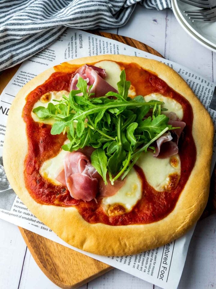 Homemade pizza with prosciutto and arugula on a wooden board with a striped napkin.