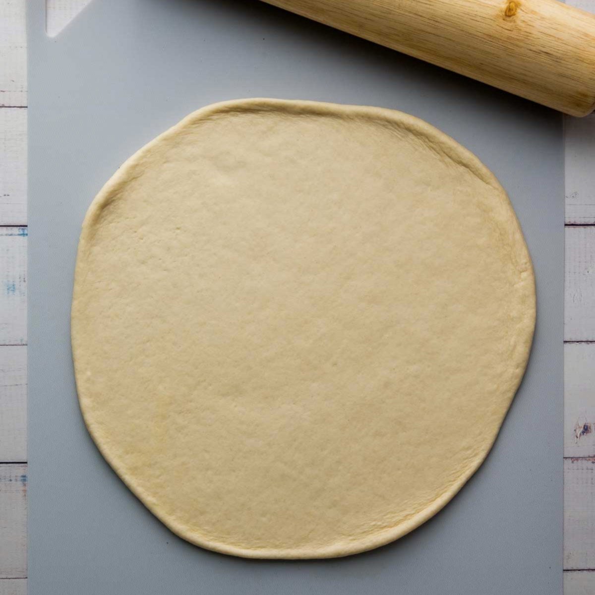 Rolled-out pizza dough on a board with a rolling pin.