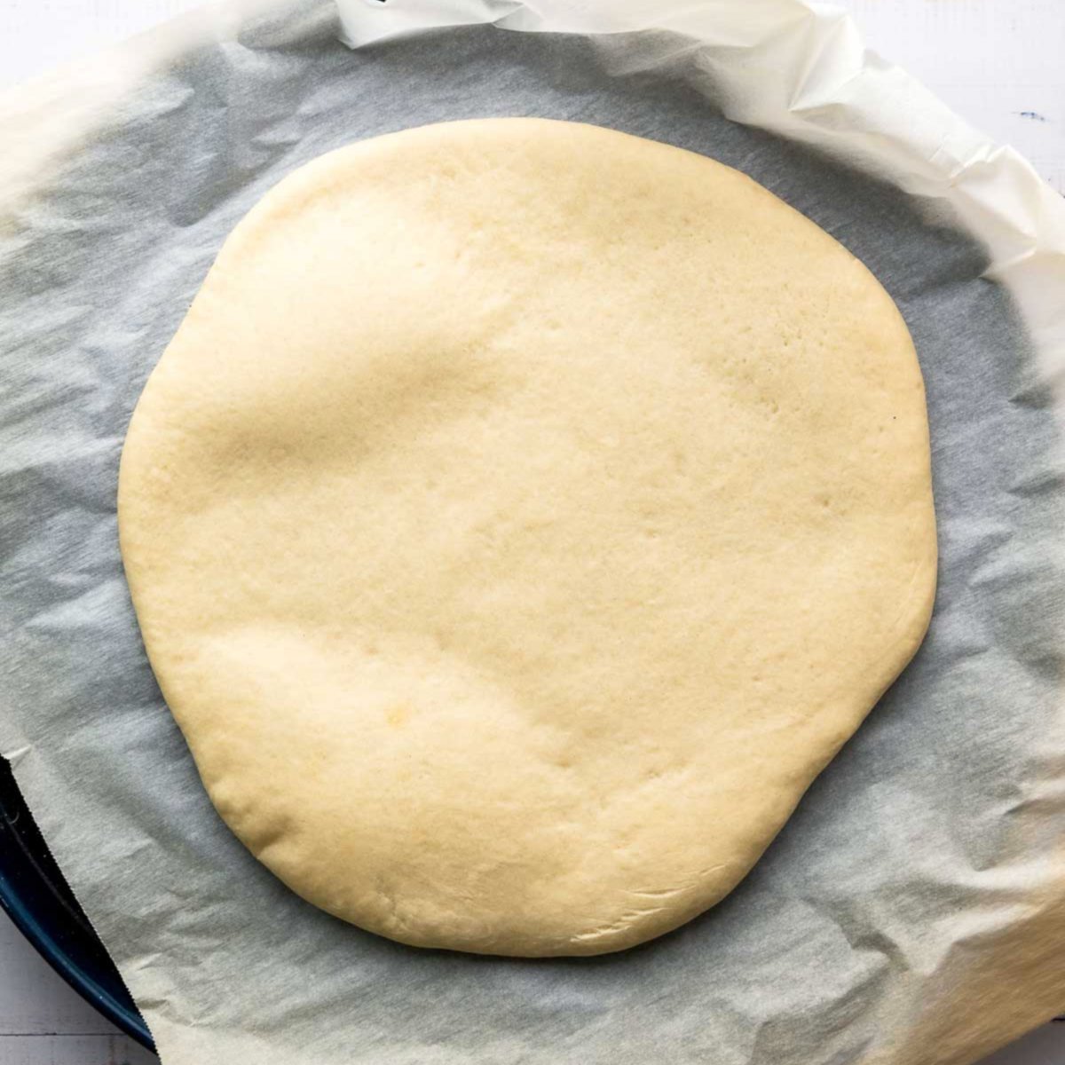 Partially baked pizza crust on parchment paper.
