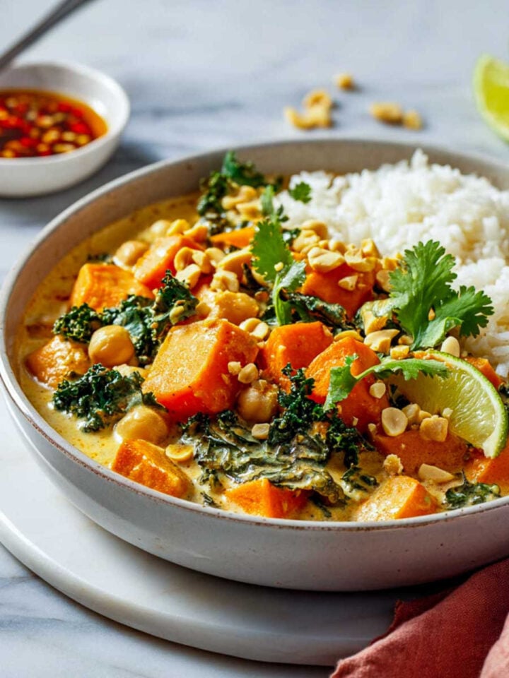 Close-up of Thai peanut stew in a shallow bowl with rice, cilantro, and lime slice.