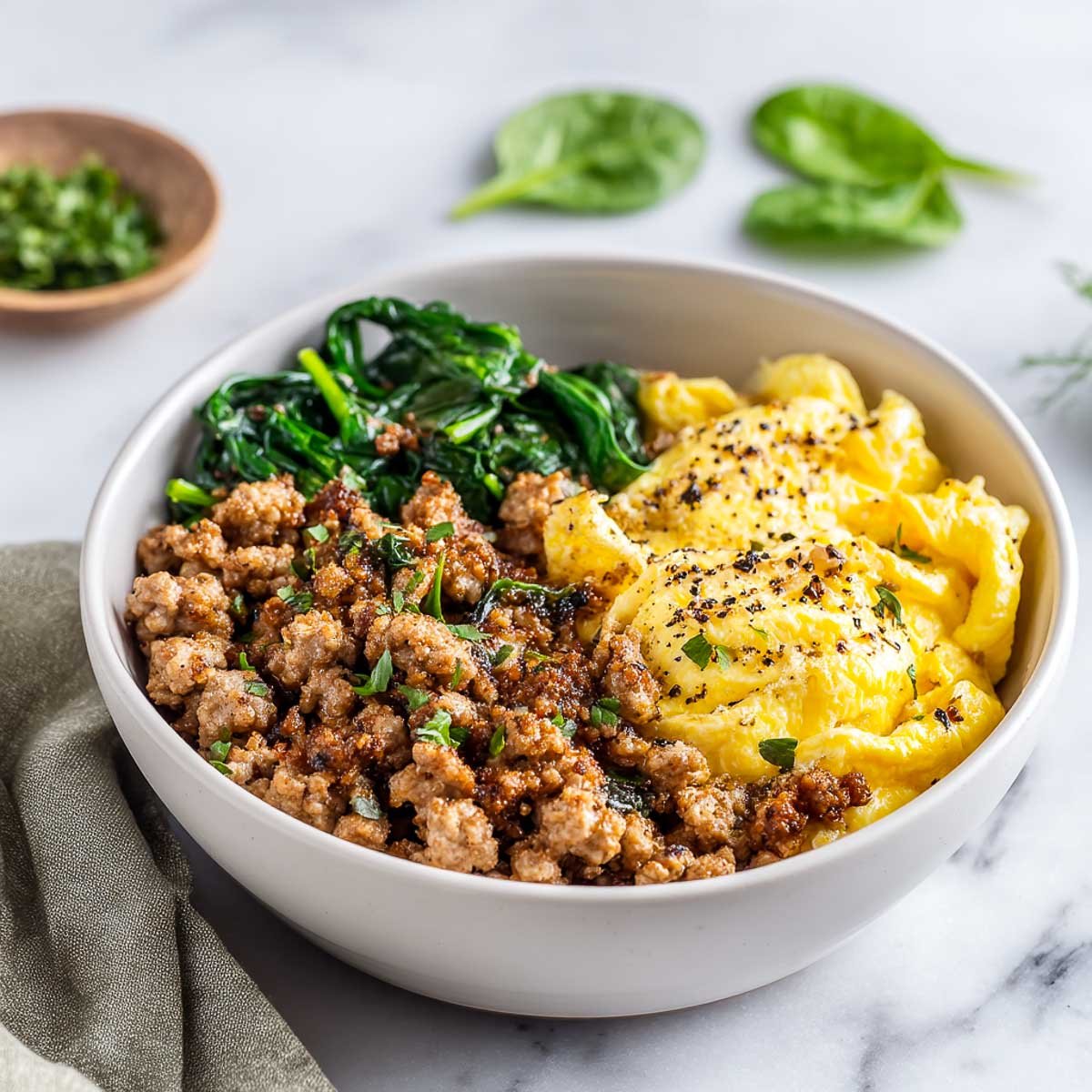 Breakfast bowl with turkey sausage, scrambled eggs, and spinach on marble for low calorie high protein breakfast.