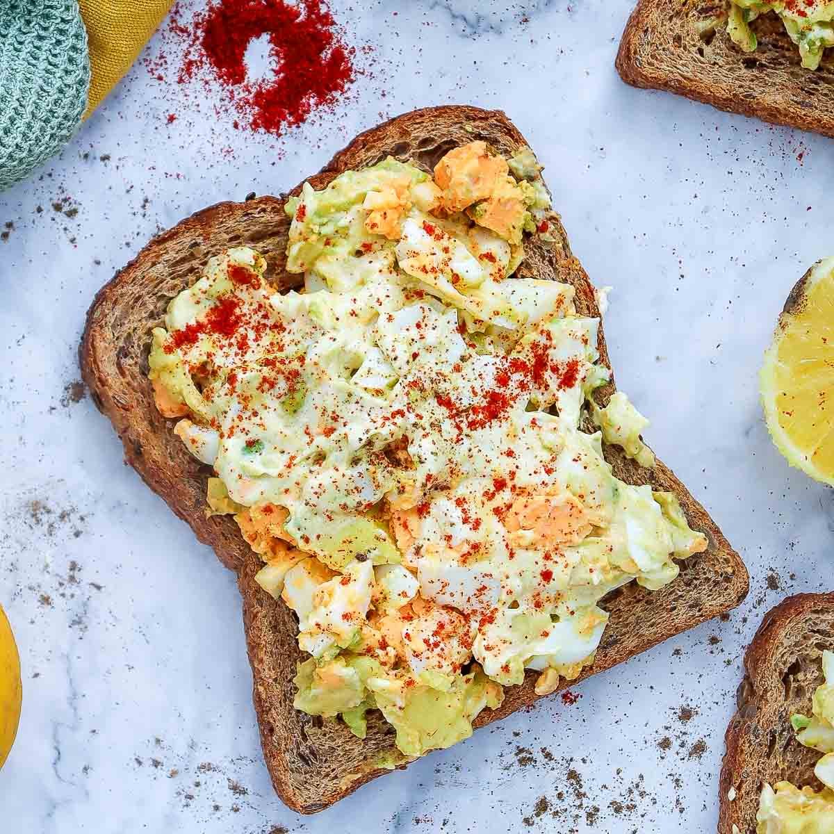 Close-up of avocado egg salad toast on whole grain bread, topped with smoked paprika.