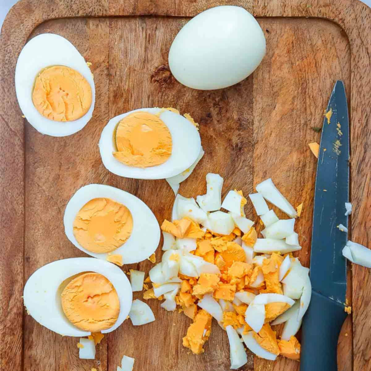 Chopped and halved hard-boiled eggs on a wooden cutting board, ready for mixing.