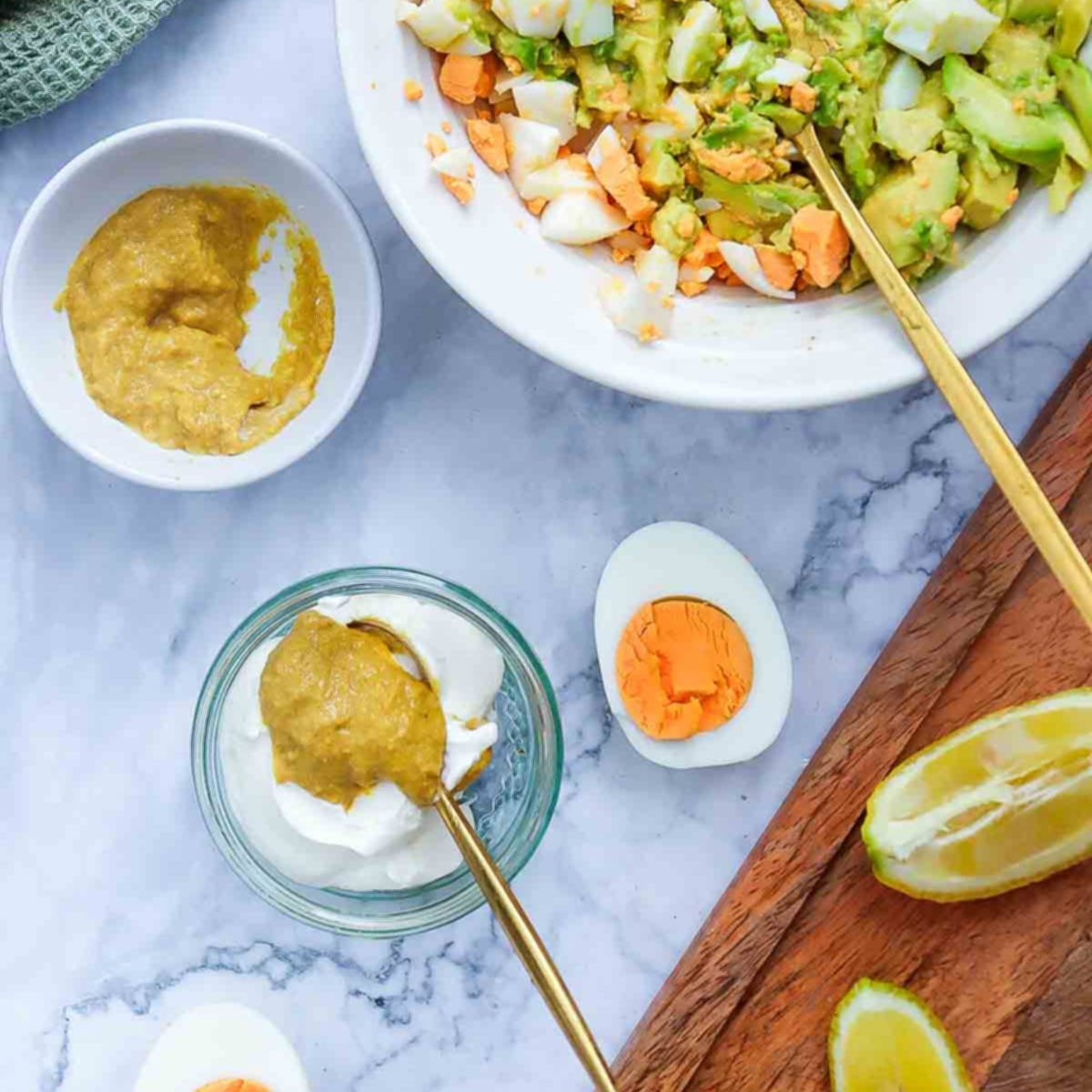 Ingredients for the dressing in small bowls, including Dijon mustard and yogurt, next to chopped eggs and avocado.
