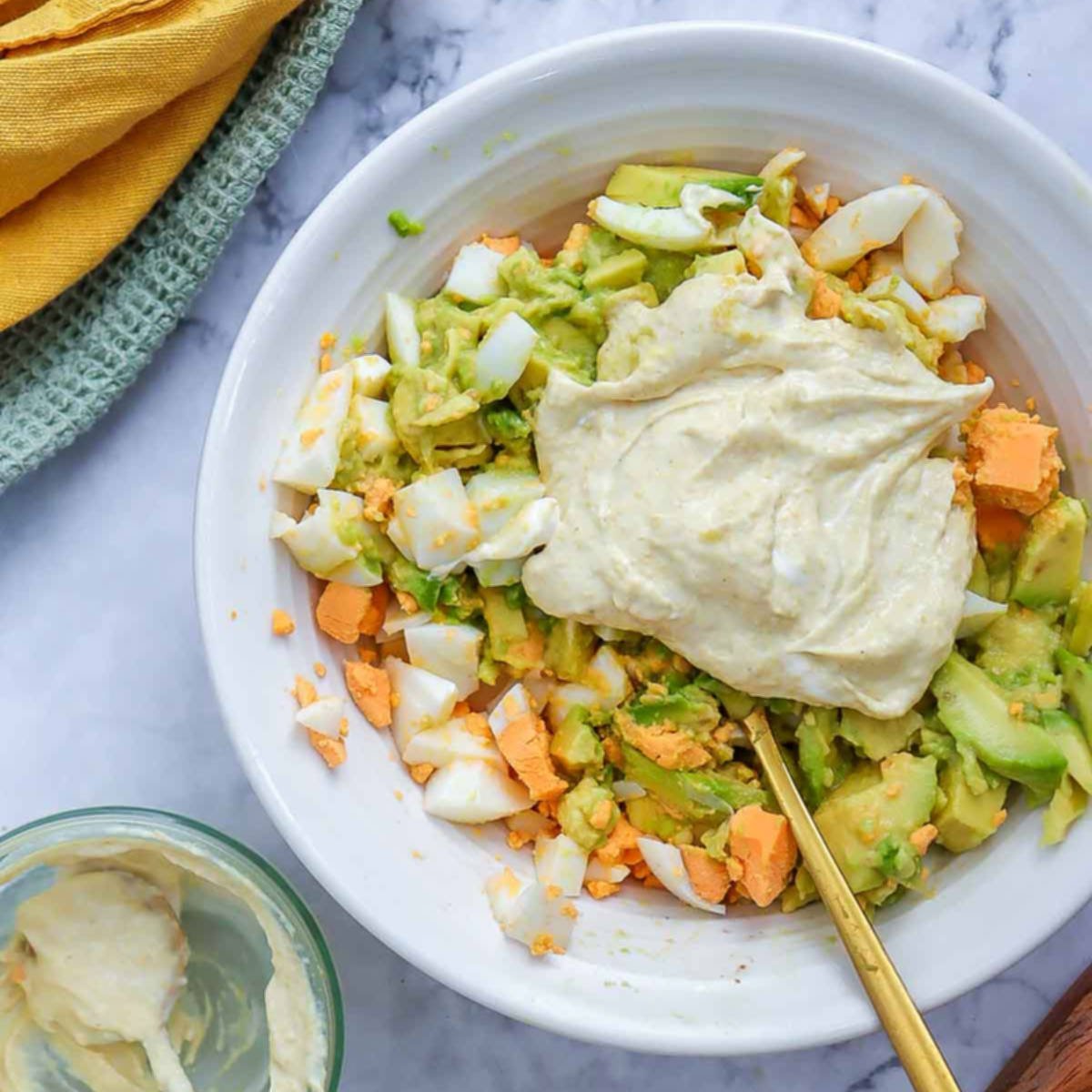 Creamy dressing added to a bowl of chopped eggs and avocado, ready to be mixed for avocado egg salad.