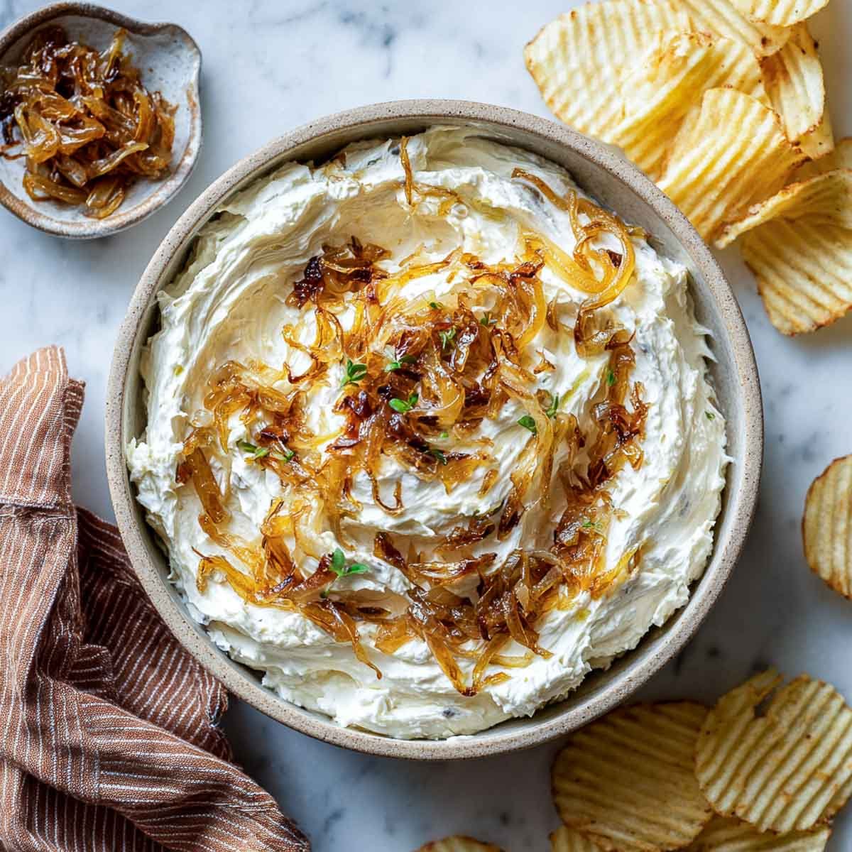 Creamy dip with caramelized onions in bowl, served with ridged potato chips.
