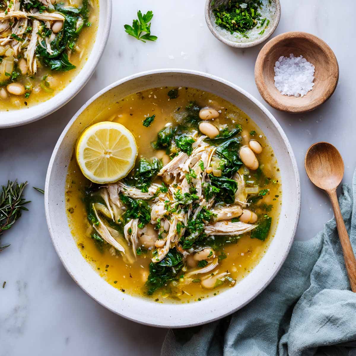 Clear chicken soup with spinach, white beans, and lemon in a white bowl.