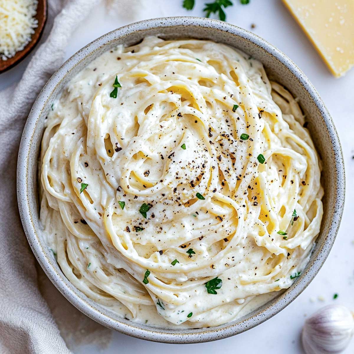 Fettuccine coated in creamy cottage cheese Alfredo sauce, garnished with parsley and pepper, next to a bowl of extra sauce.