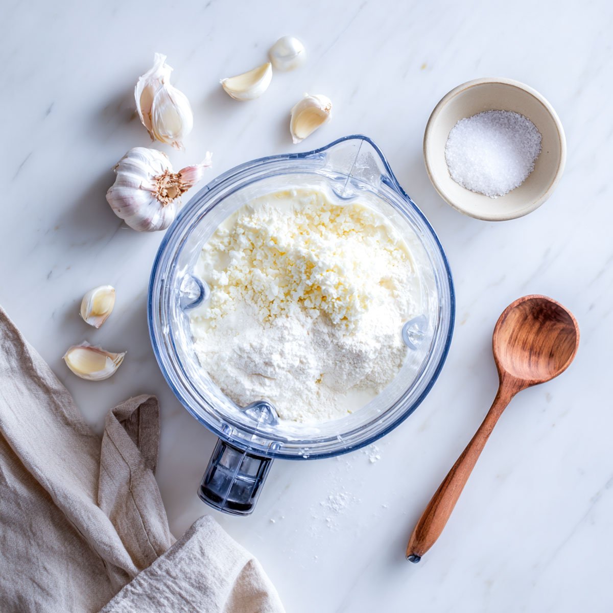 Cottage cheese, Parmesan, milk, and cornstarch layered in a blender before blending into Alfredo sauce, with garlic and salt nearby.