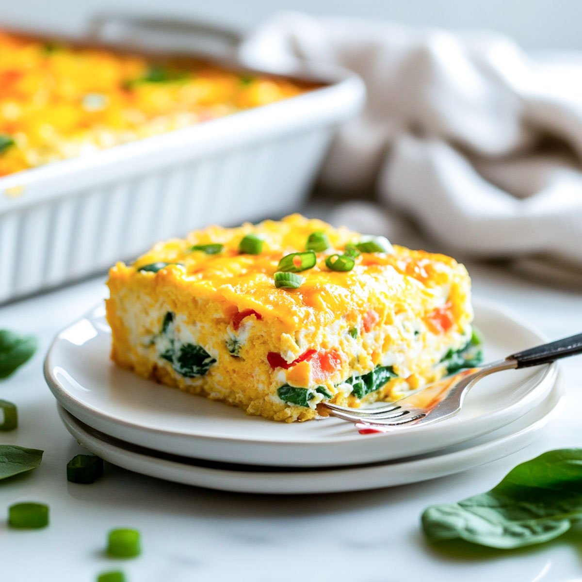 Single plated serving of cottage cheese egg casserole on stacked white plates, showing layers of spinach, peppers, and melted cheese, with the baking dish in the background.