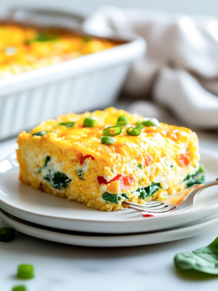 Close-up of a single slice of cottage cheese egg casserole on a plate with a fork, highlighting the creamy, cheesy interior with visible spinach and peppers.