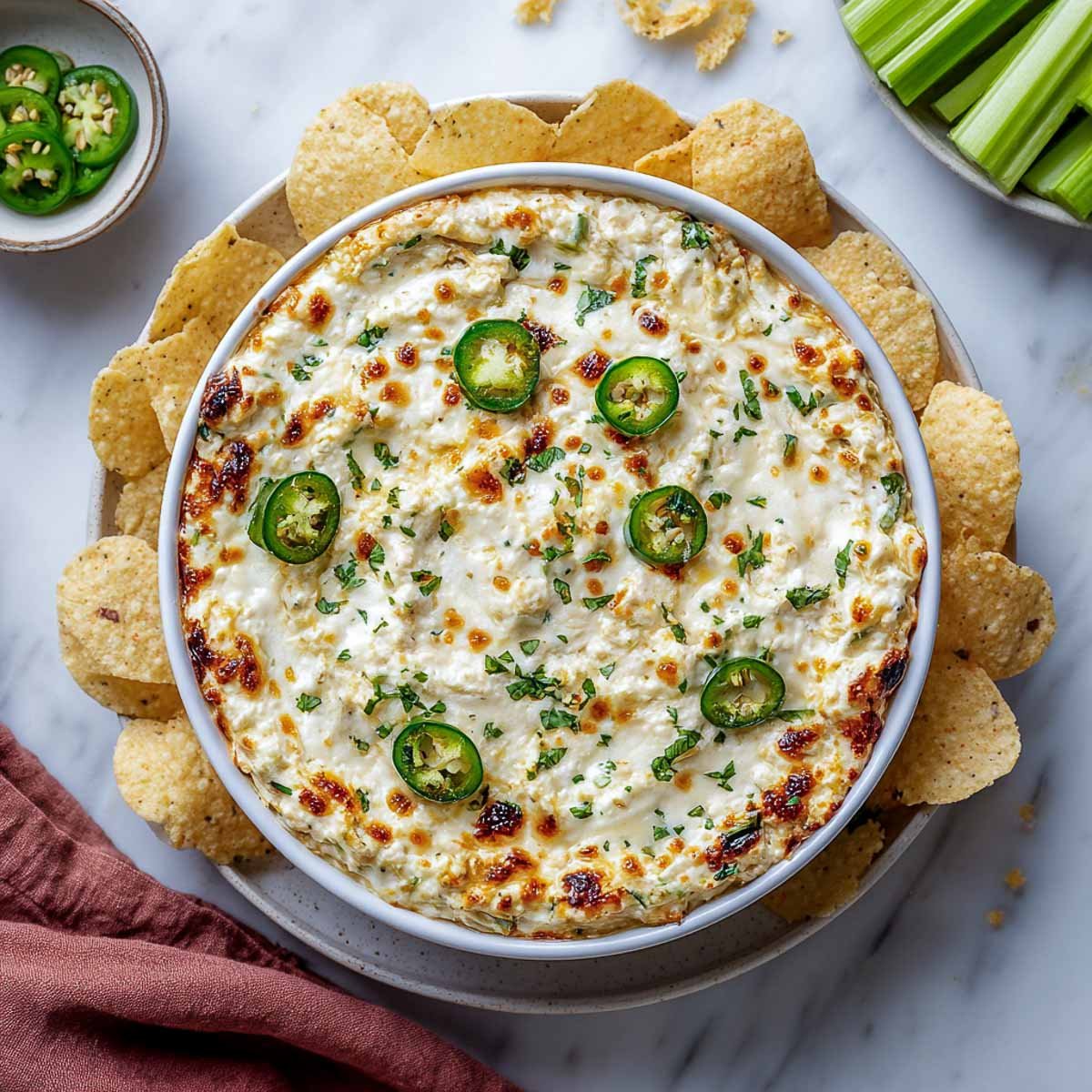 Cheesy jalapeño dip topped with sliced peppers, served with chips and celery.
