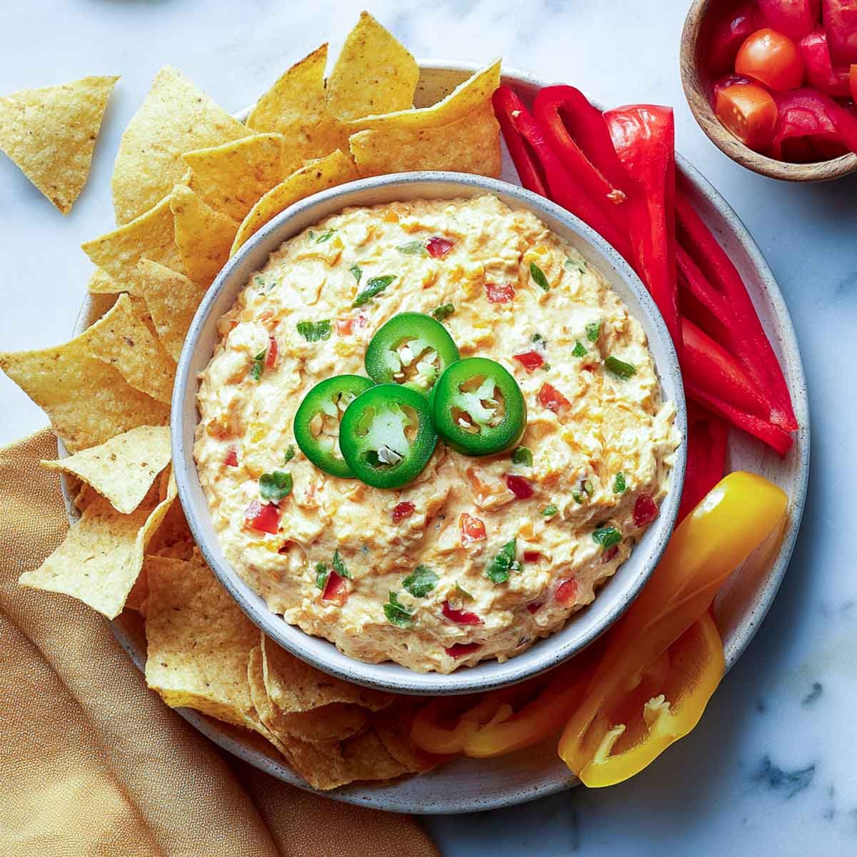 Warm queso dip with jalapeño slices, surrounded by chips and bell pepper strips.