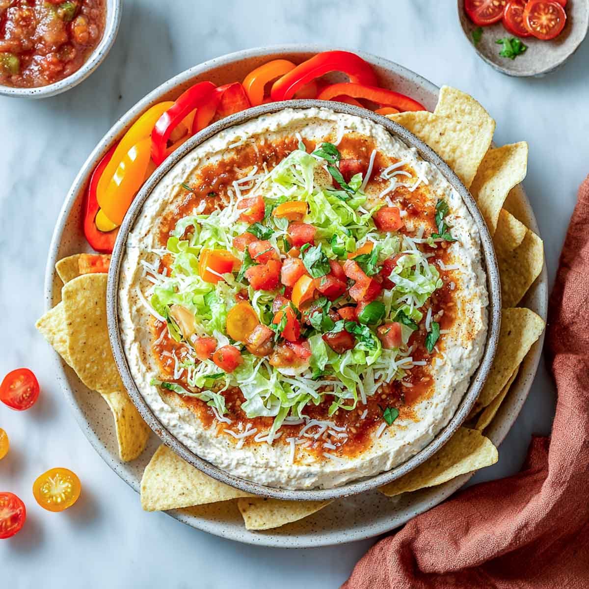 Layered taco dip with salsa, lettuce, and tomatoes served with chips and peppers.