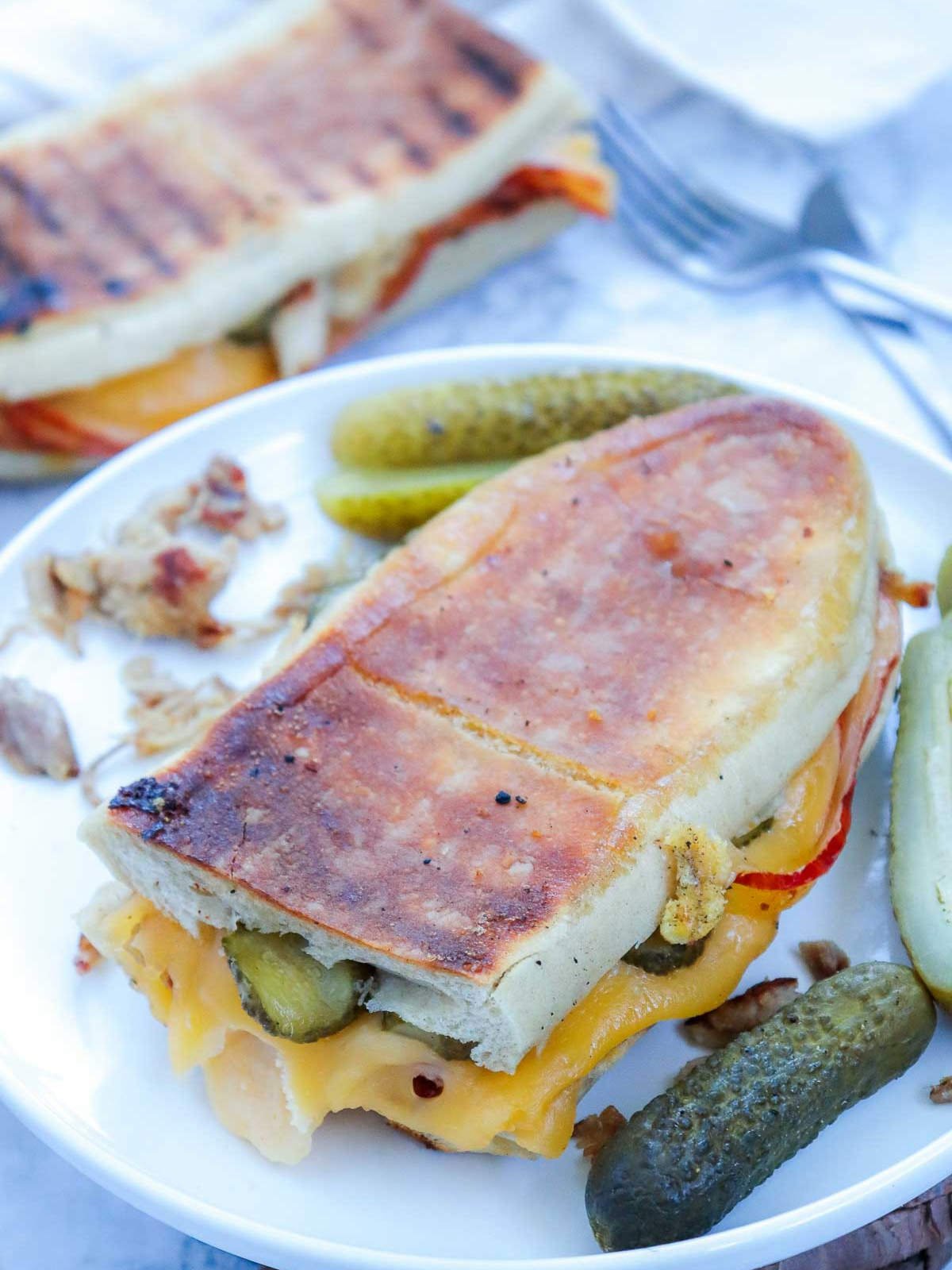 Crispy Cuban sandwich served with dill pickles and pulled pork pieces on the plate.