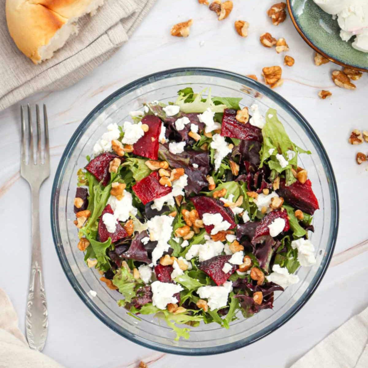 Overhead view of beet and goat cheese salad in a glass bowl with chopped walnuts and mixed greens.
