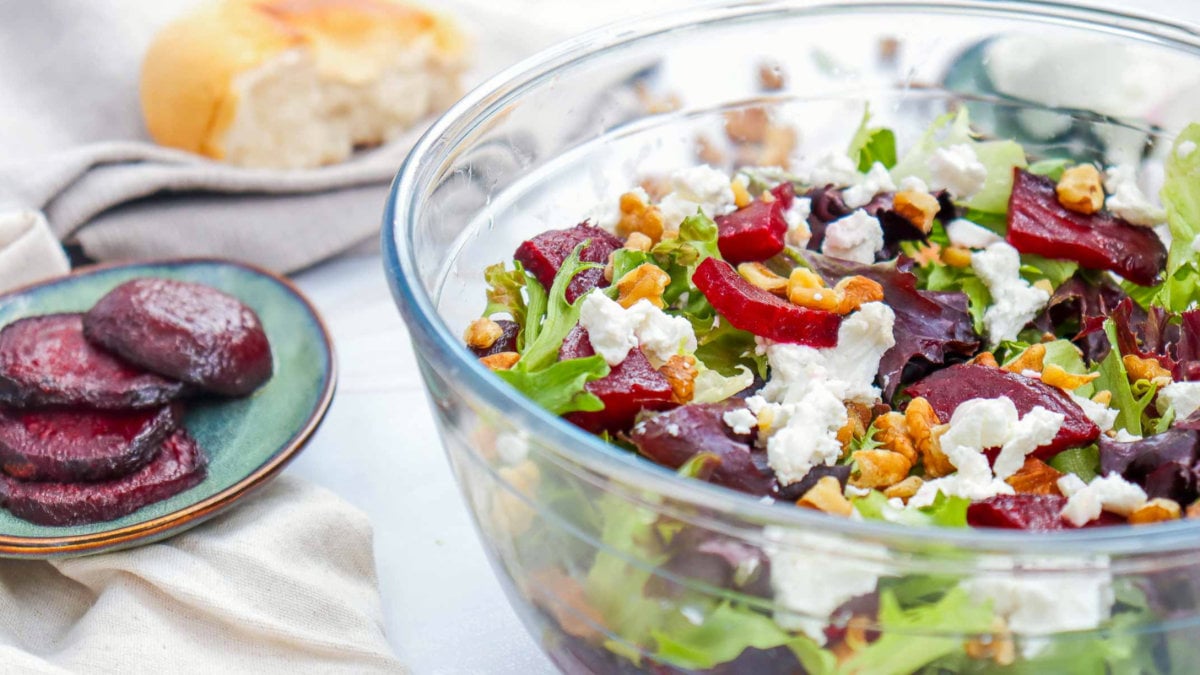 Side view of beet salad in a glass bowl with sliced beets, crumbled goat cheese, and leafy greens.