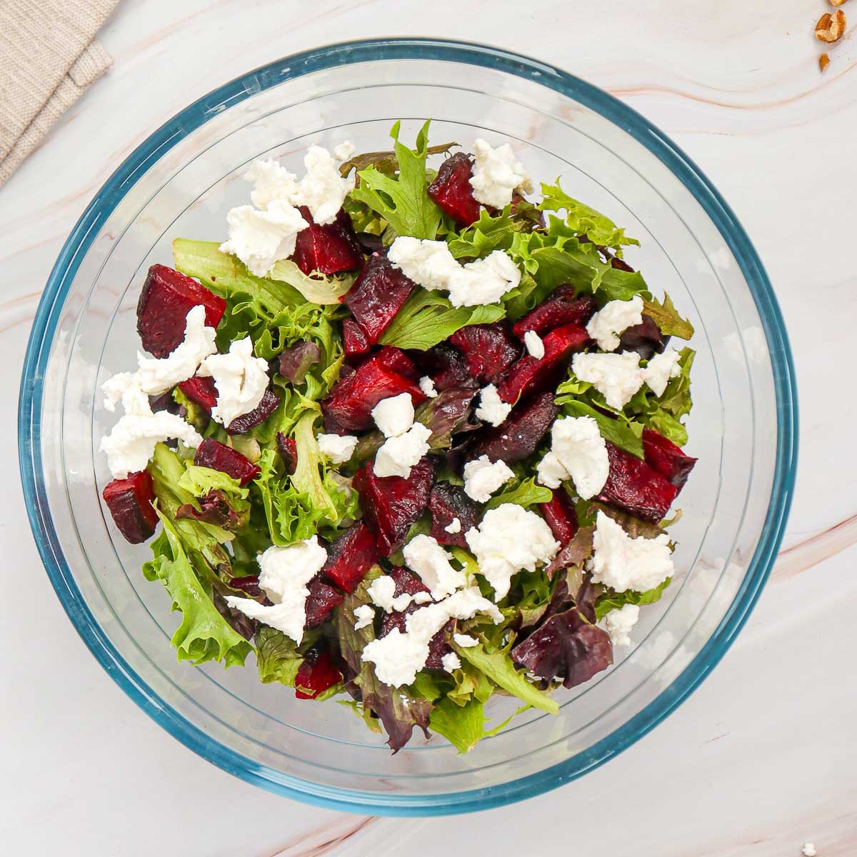 Assembling the salad in a glass bowl with mixed greens.
