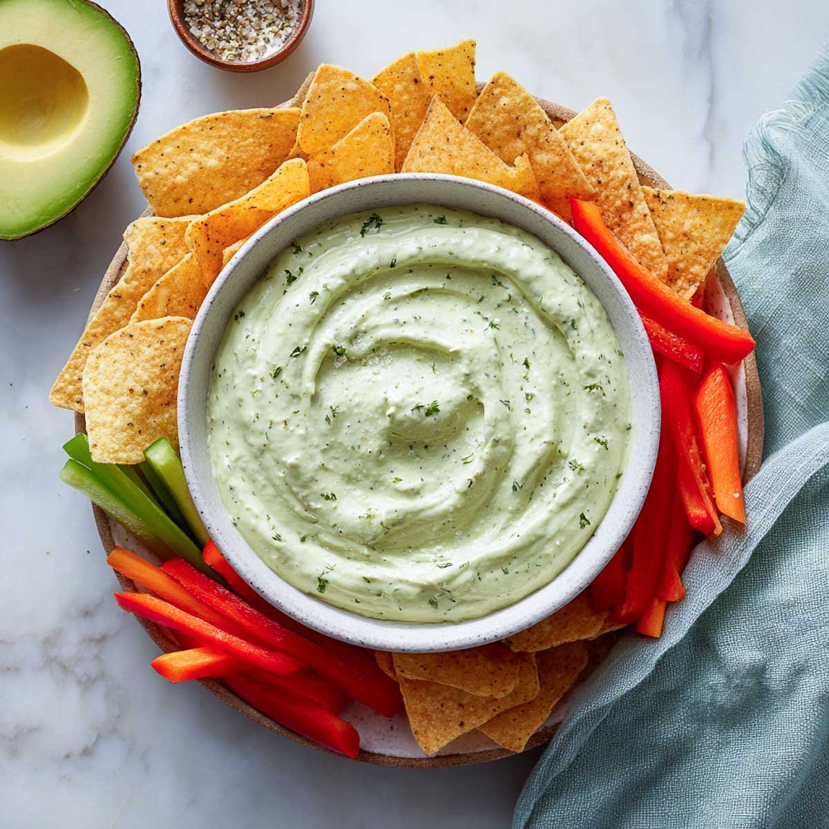 Avocado ranch dip with herbs served with chips, bell pepper strips, and celery.
