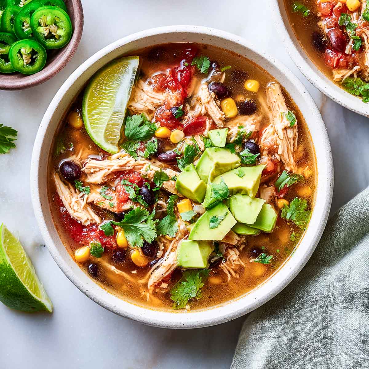 Brothy chicken taco soup with corn, black beans, avocado, and lime.