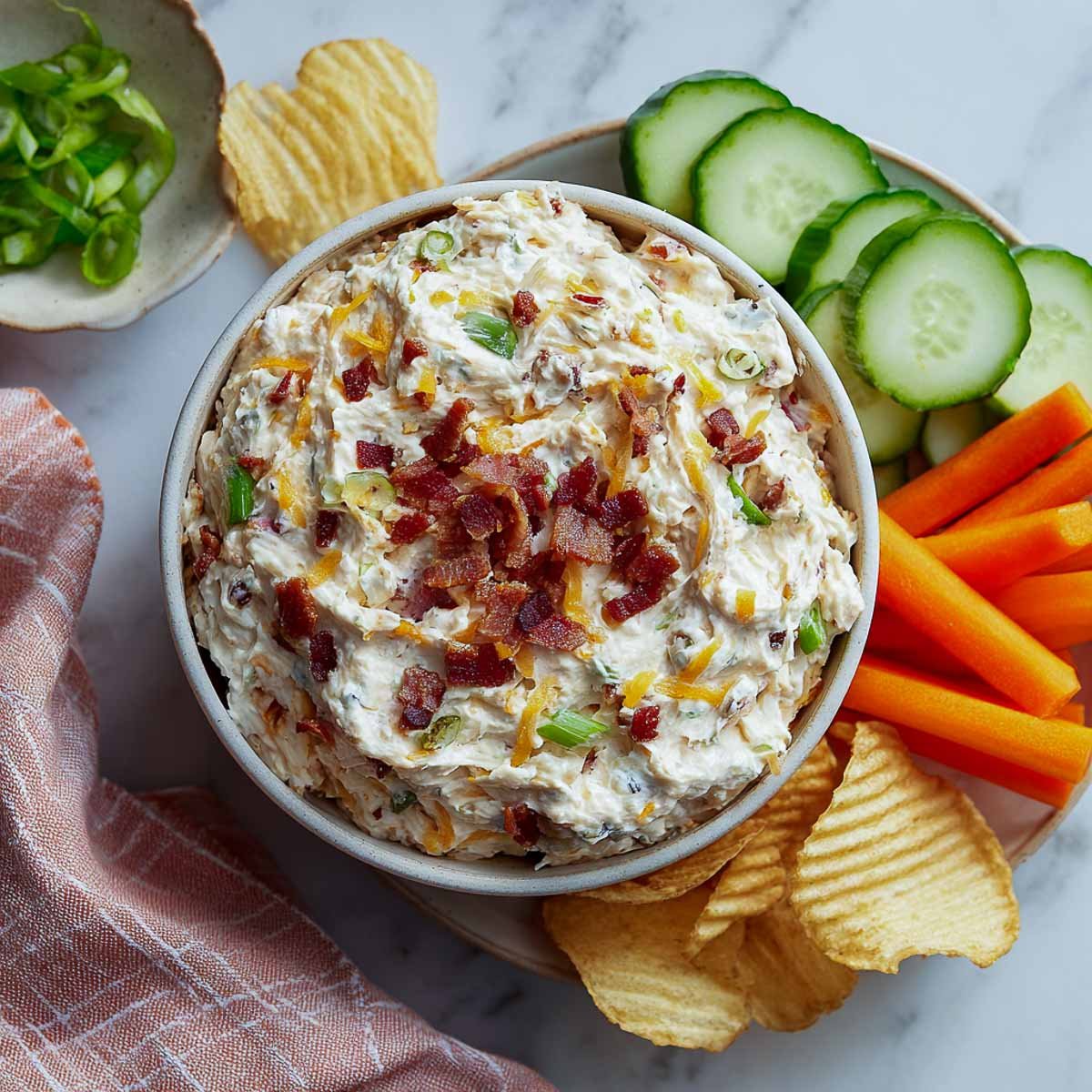 Creamy dip with bacon, cheese, and green onions in a bowl with chips.