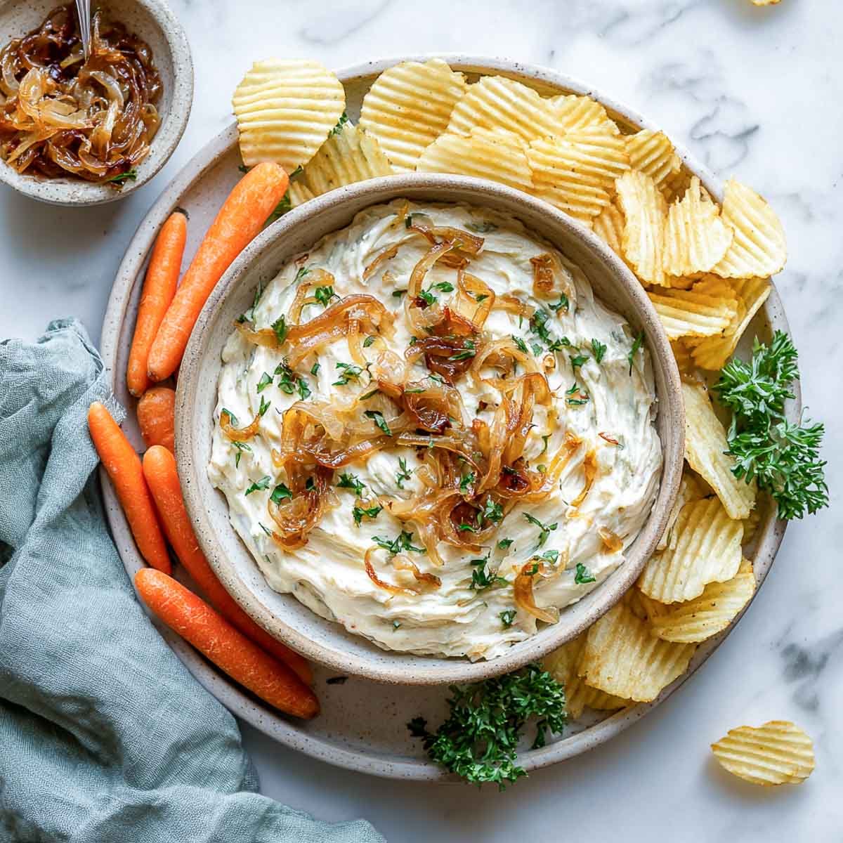 Creamy French onion dip topped with caramelized onions, served with chips and carrots.
