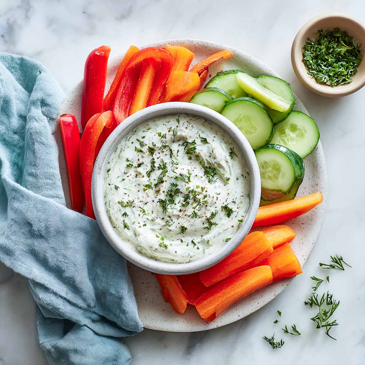 Creamy ranch dip with herbs served with bell pepper, carrot, and cucumber slices.