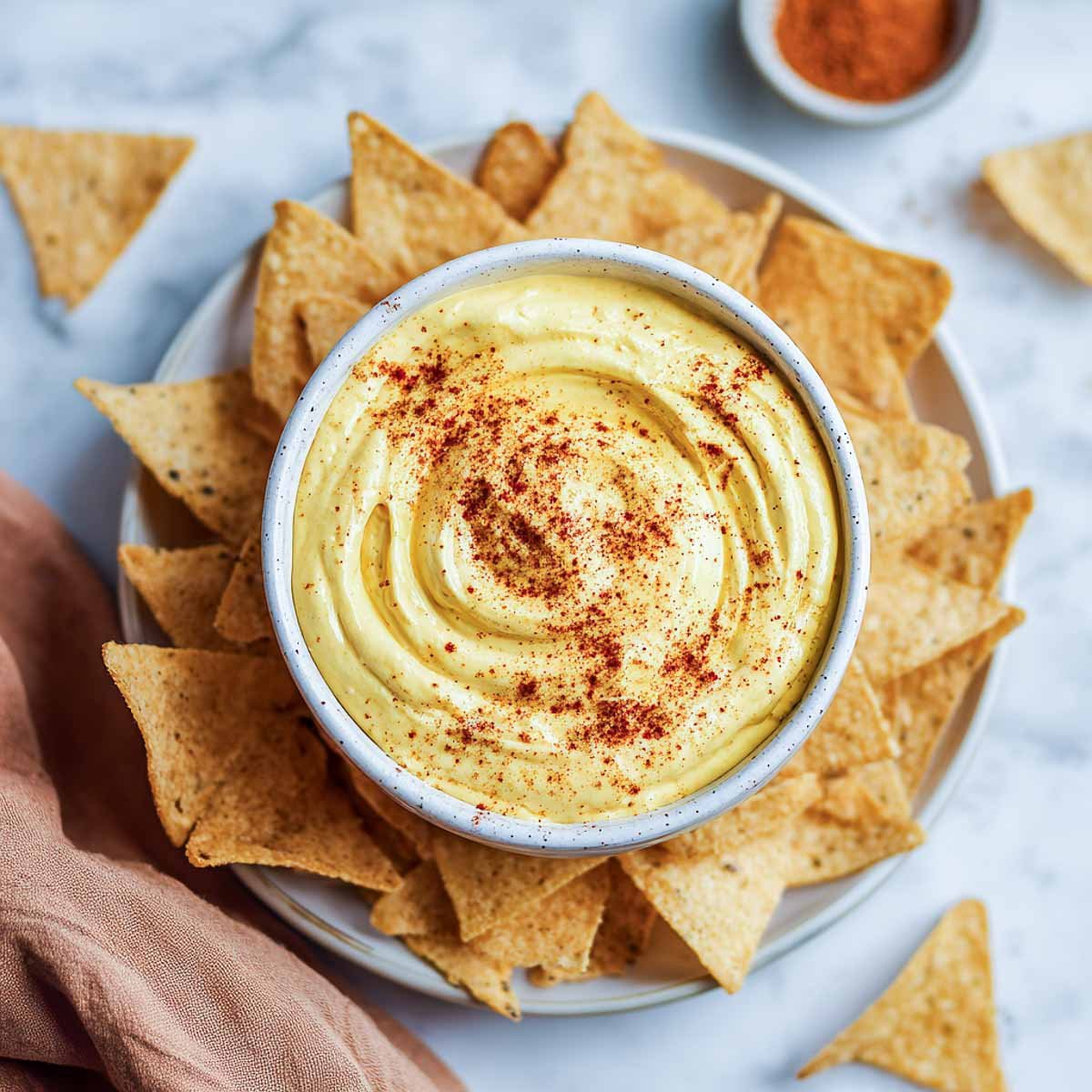 Creamy yellow nacho dip with taco seasoning and tortilla chips on the side.