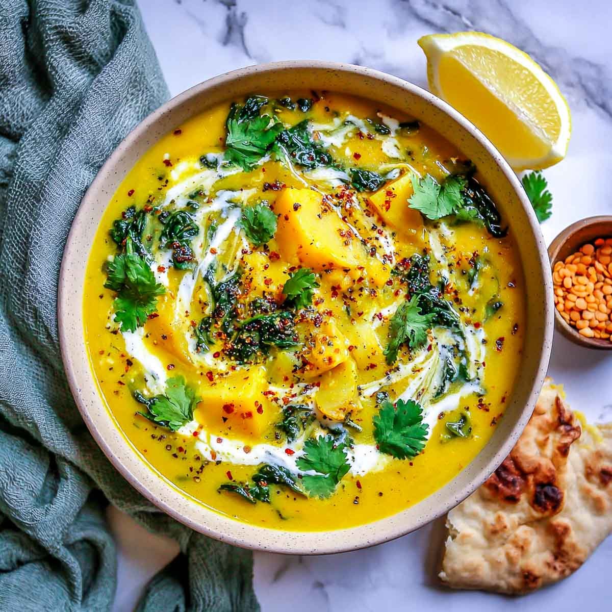 Top-down view of golden turmeric veggie soup with potatoes, lentils, and greens.
