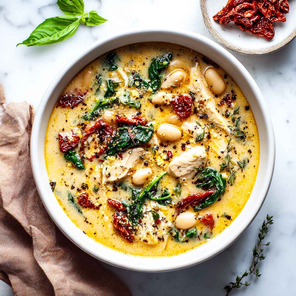 Top-down view of creamy Tuscan chicken soup with white beans, spinach, and sun-dried tomatoes.