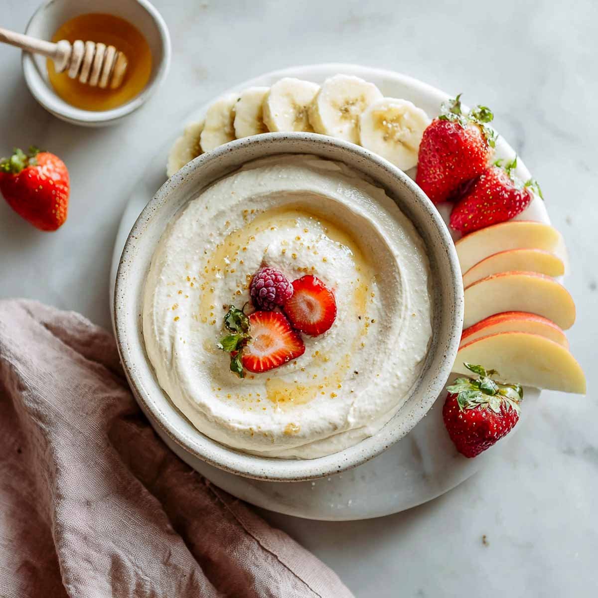 Creamy fruit dip with honey swirl served with apple slices, bananas, and berries.