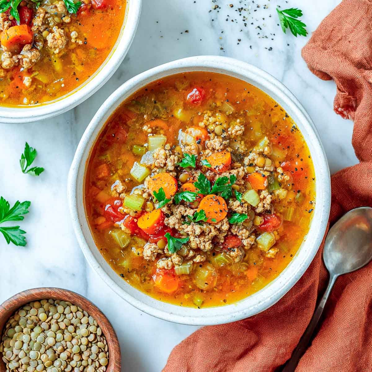 Chunky turkey and lentil soup with carrots and celery in a white bowl.