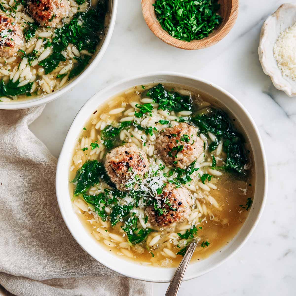 Brothy Italian wedding soup with turkey meatballs, orzo, and spinach in a white bowl.