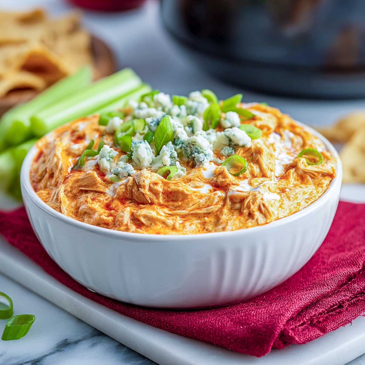 Top-down view of buffalo chicken dip with cheese, scallions, and blue cheese crumbles.