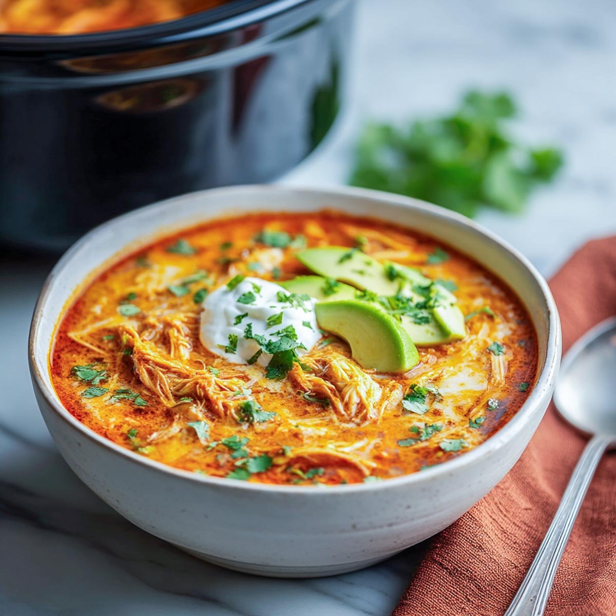 Creamy chicken enchilada soup in a white bowl with avocado, sour cream, and cilantro.