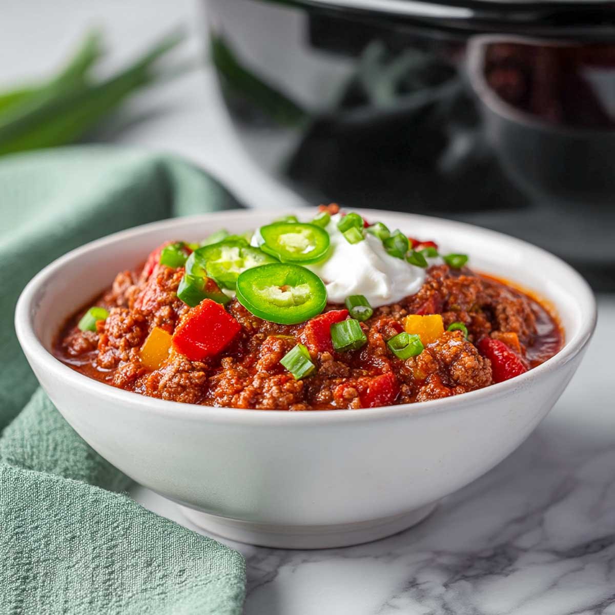 Chunky keto chili in a black crockpot with wooden spoon and cilantro garnish.