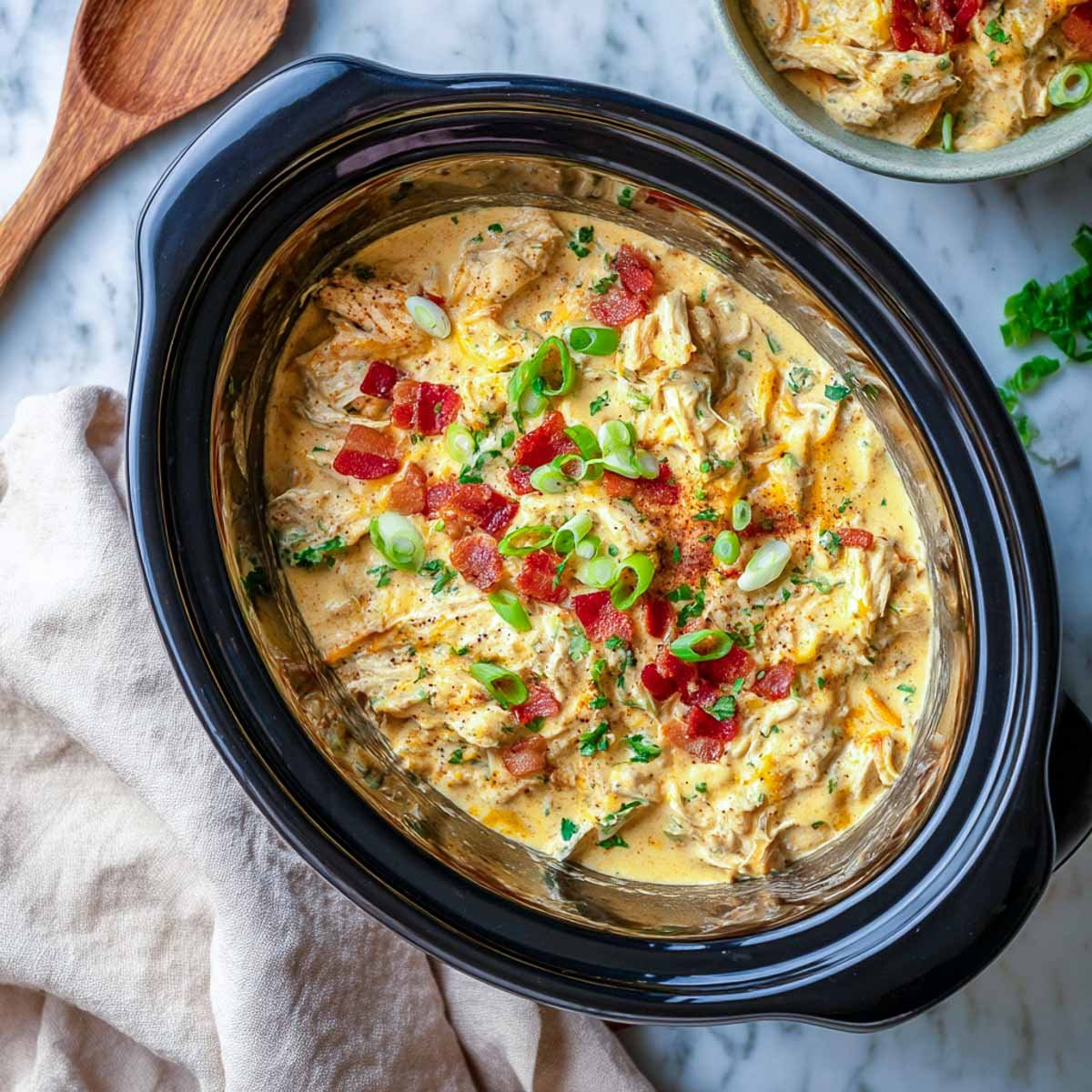 Cheesy crack chicken in crockpot with beige napkin and bowl behind.