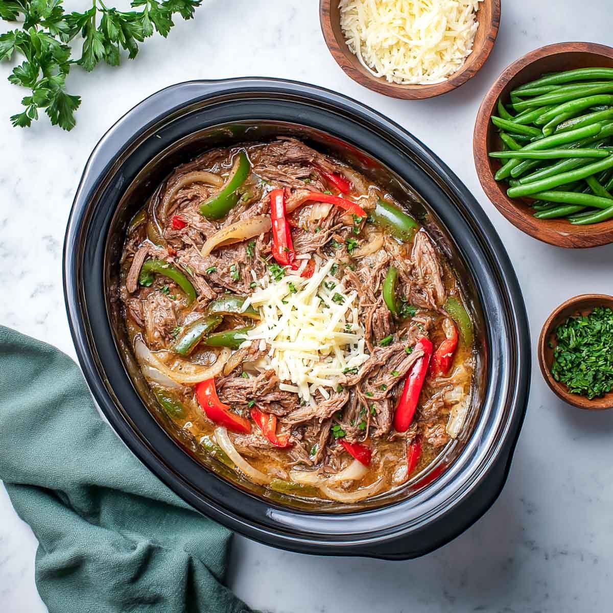 Top-down view of keto crockpot Philly cheesesteak meat with melted cheese, peppers, and onions.